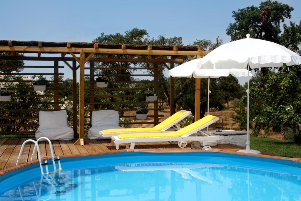 ein Pool mit zwei gelben Stühlen, einem Regenschirm und einem Sonnenschirm in der Unterkunft Monte da Casa Branca by Hi Alentejo in São Bartolomeu da Serra