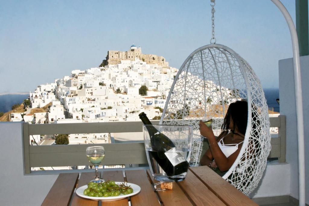 Anatoli Luxury Studios & Suites في مدينة أستيباليا: امرأة تجلس على أرجوحة على طاولة مع زجاجة من النبيذ