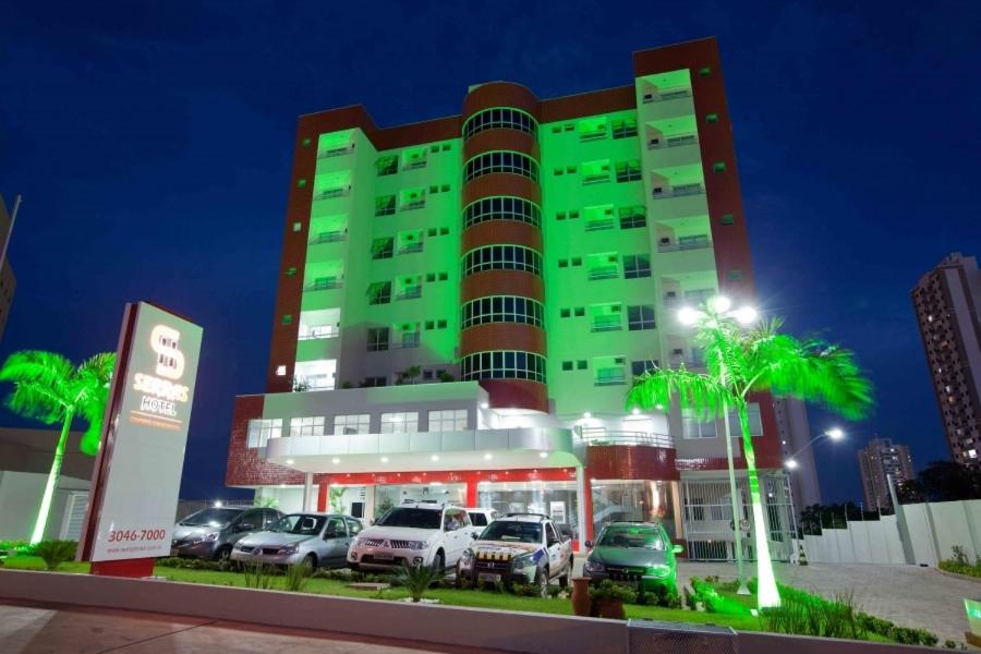 a green building with cars parked in a parking lot at Serras Hotel in Cuiabá