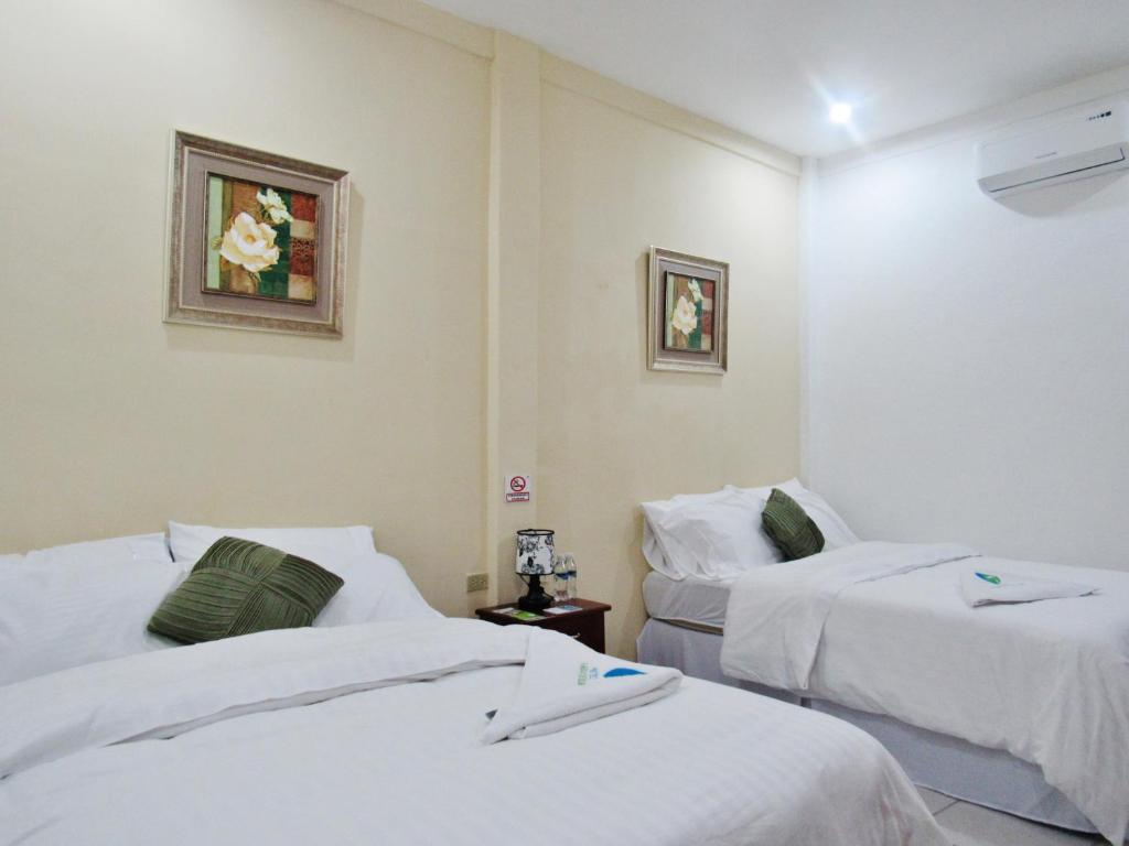 two beds in a room with white sheets at Hotel Palmeras de Elim in Matagalpa