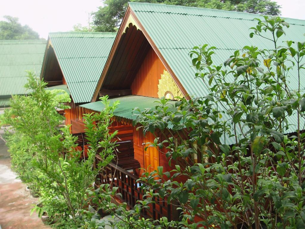 una pequeña casa con un techo verde detrás de algunos árboles en Baan Kong Homestay, en Phra Nakhon Si Ayutthaya