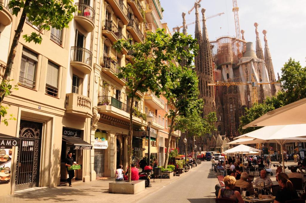 una calle de la ciudad con gente sentada en mesas y edificios en Gaudi Sagrada Familia en Barcelona