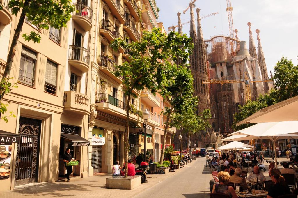 una via cittadina con persone sedute ai tavoli e agli edifici di Gaudi Sagrada Familia a Barcellona