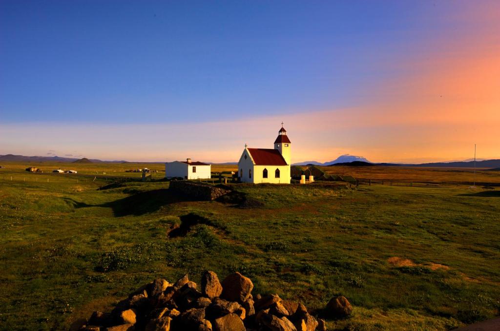 a church in the middle of a field with a sunset at Fjalladýrð Guesthouse in Modrudalur