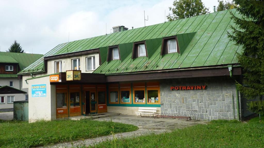 un edificio con techo verde y un banco delante de él en Penzion Tendr, en Deštné v Orlických horách