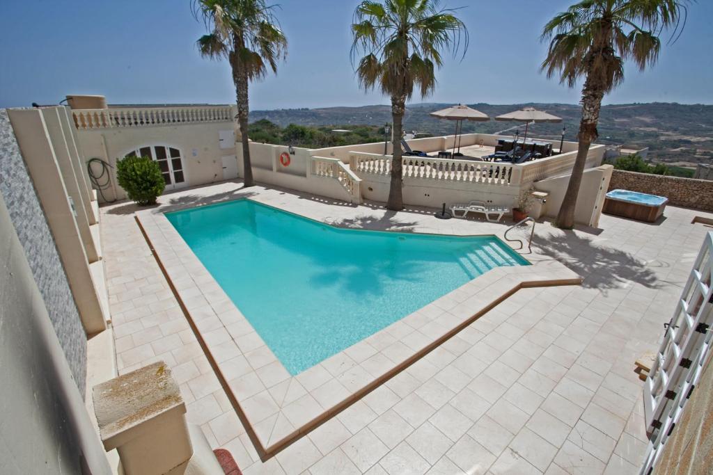 a swimming pool in a backyard with palm trees at Villa Bernardette in Xagħra