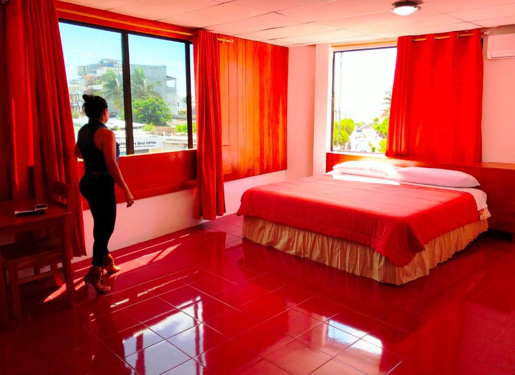 Eine Frau, die aus dem Fenster eines roten Schlafzimmers schaut. in der Unterkunft Hostal Muyuyo in Puerto Ayora