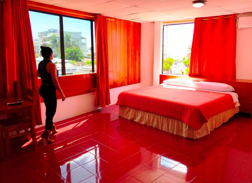 a woman looking out the window of a red bedroom at Hostal Muyuyo in Puerto Ayora