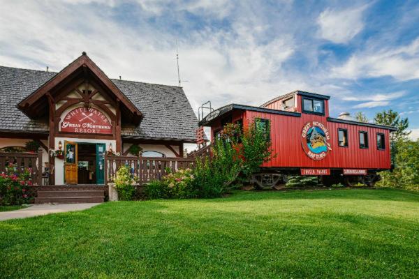 Great Northern Resort (Lodge) في ويست غلاسير: سيارة قطار حمراء متوقفة أمام مبنى