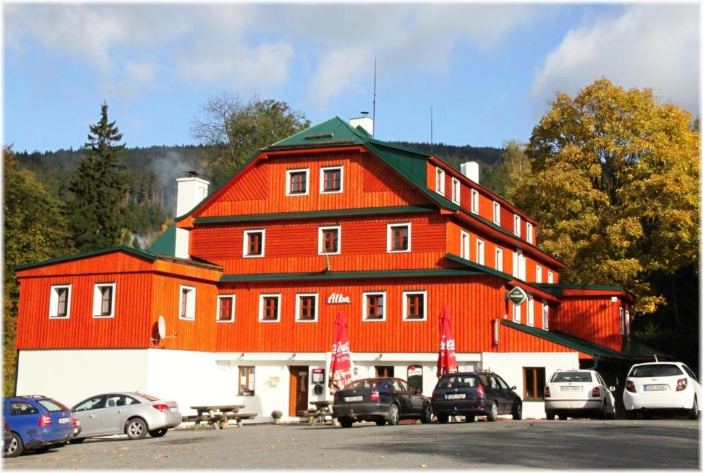 duży czerwony budynek z samochodami zaparkowanymi na parkingu w obiekcie Hotel Alba w mieście Deštné v Orlických horách