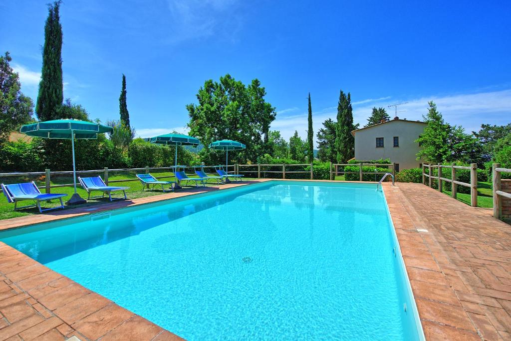 uma piscina com cadeiras azuis e guarda-sóis em Villa Picchio by PosarelliVillas em Volterra