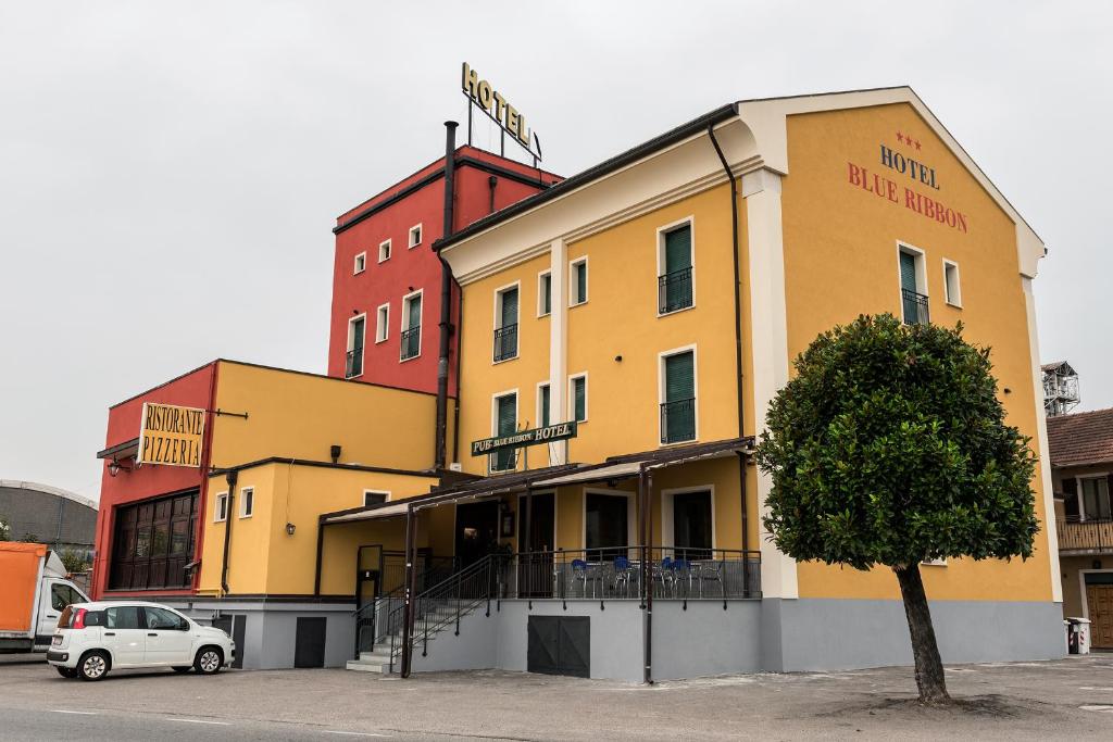 a yellow building with a tree in a parking lot at Hotel Blue Ribbon in Vercelli