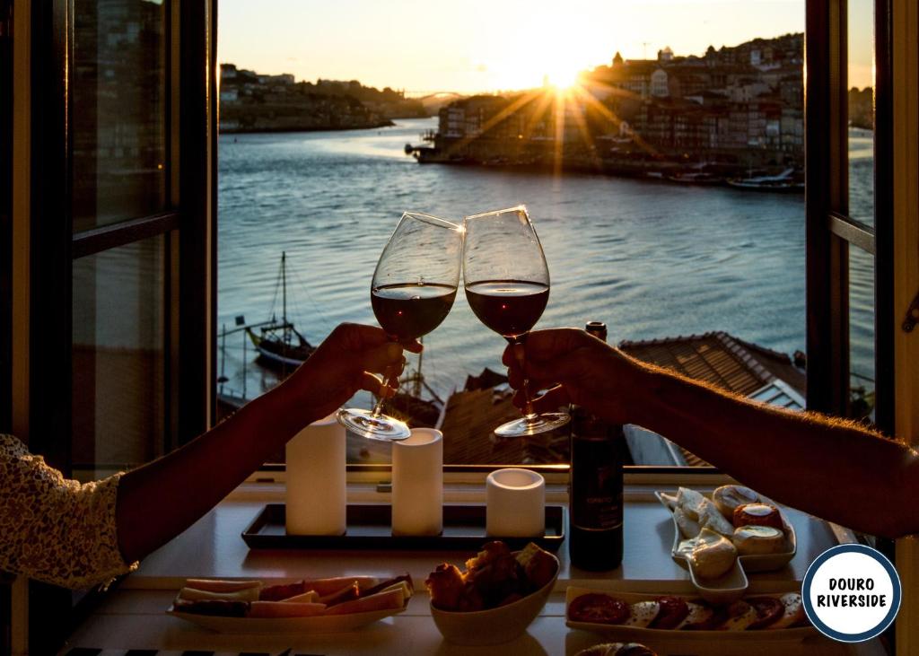 two people holding glasses of wine in front of a window at Douro Riverside Apartments in Vila Nova de Gaia