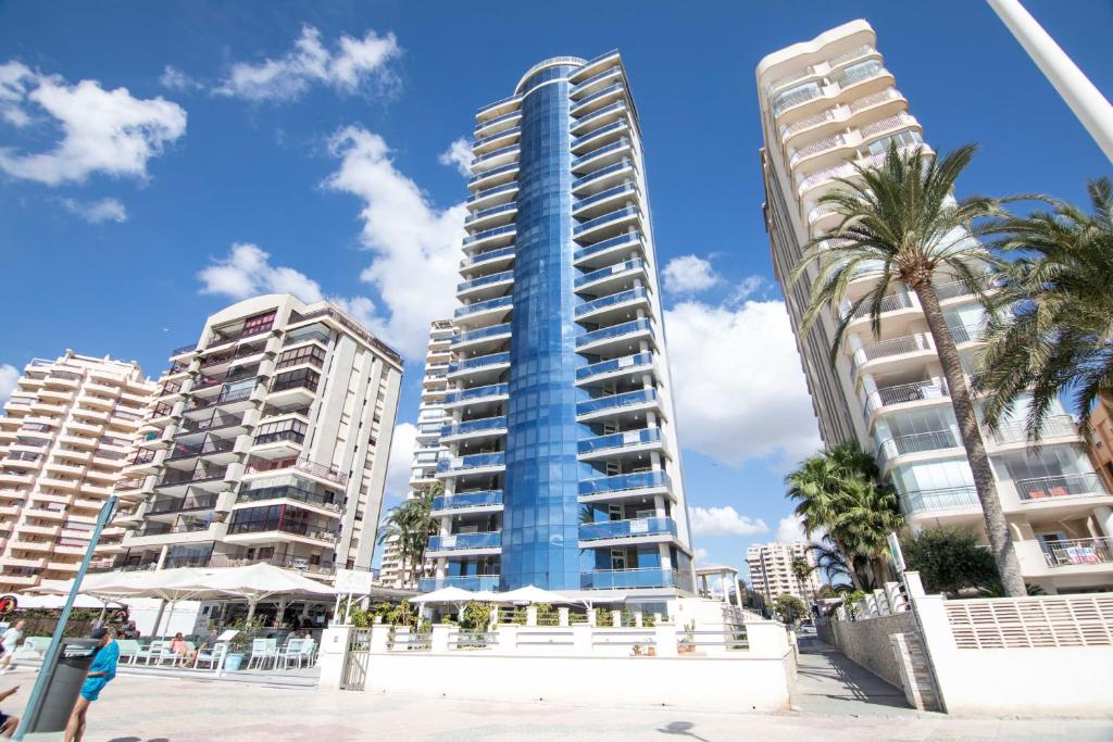 un edificio alto en la playa con palmeras y edificios en Apartamentos Vista Bella, en Calpe