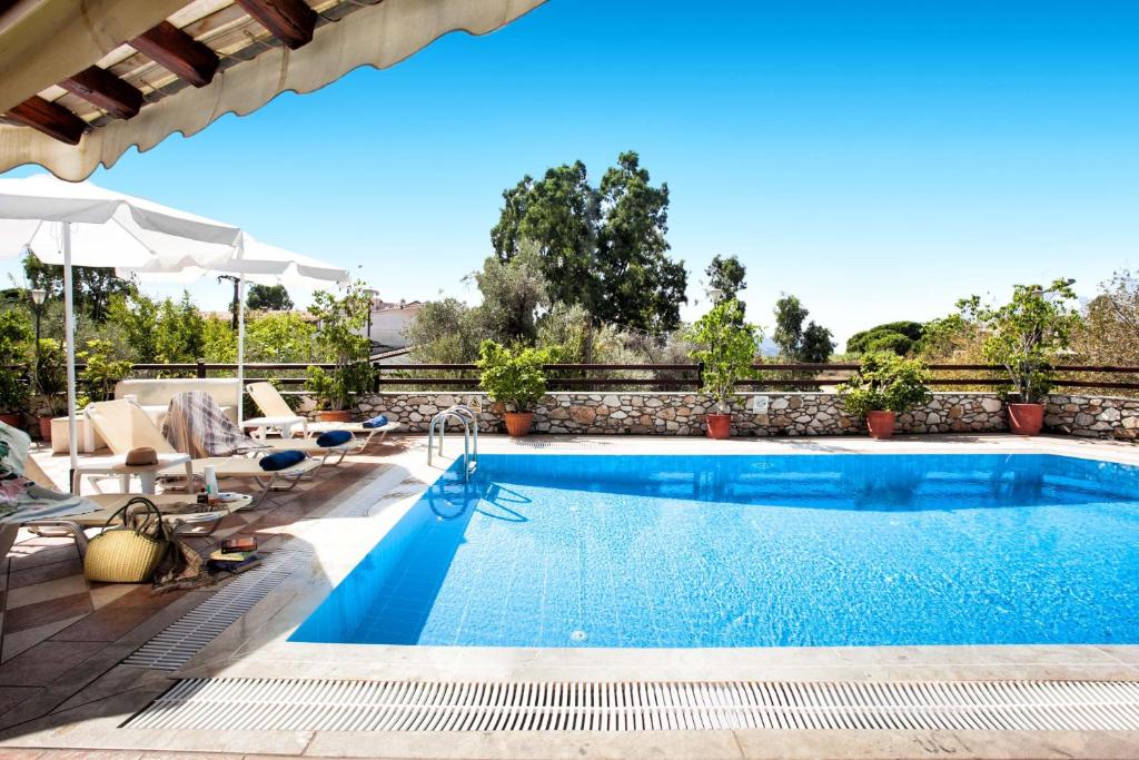 a swimming pool with chairs and an umbrella next to a patio at Villa Maraki in Agia Paraskevi
