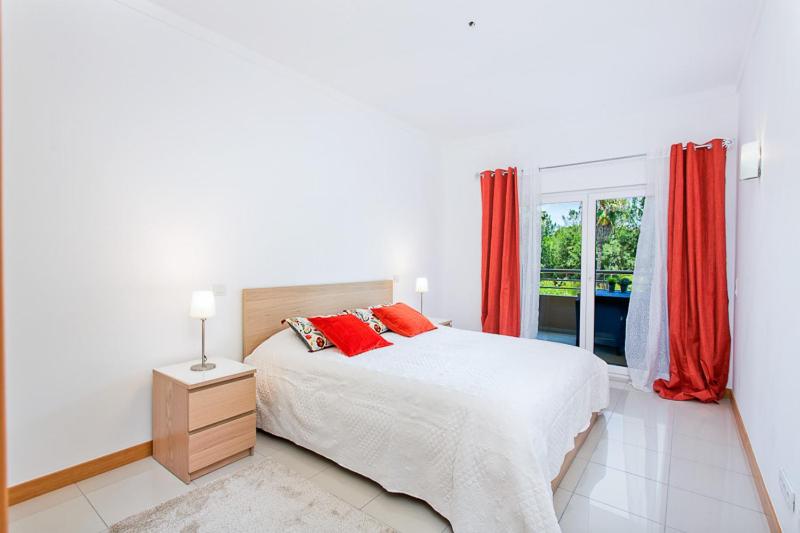 sypialnia z łóżkiem z czerwonymi zasłonami i oknem w obiekcie Apartamento em Quinta da Barracuda w Albufeirze