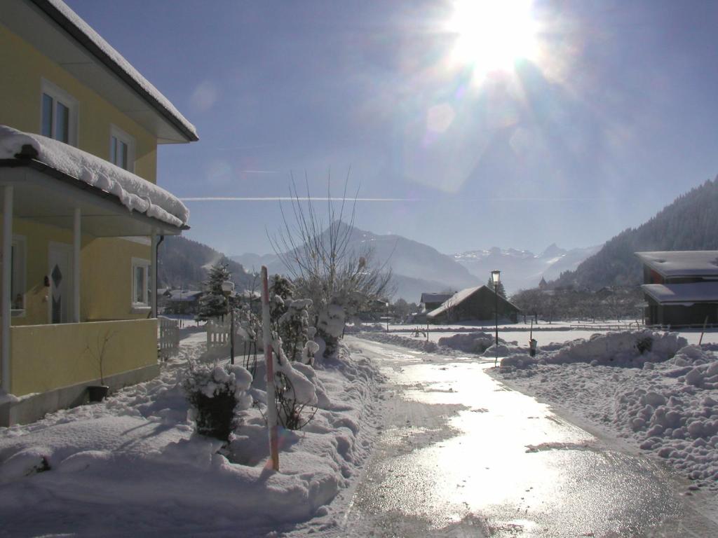 a snow covered road next to a house with the sun at Haus Pfeiffenberger in Eben im Pongau