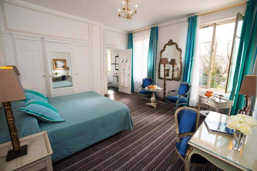 een slaapkamer met een blauw bed en een tafel en stoelen bij Pavillon Henri IV - Hotel Restaurant Terrasse in Saint-Germain-en-Laye