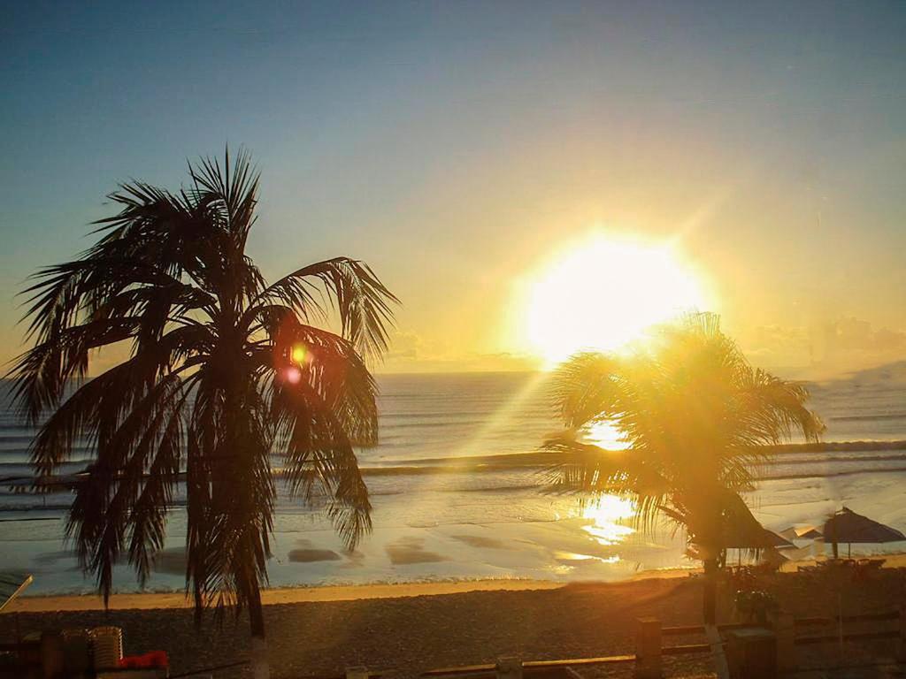 una puesta de sol en una playa con dos palmeras en POUSADA TIA LUCY, en Natal