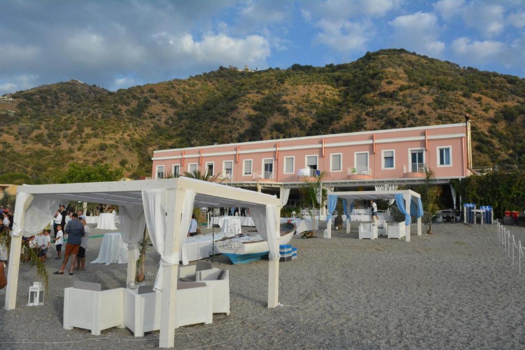 un bâtiment rose avec des tables et des chaises devant un bâtiment dans l'établissement Hotel Ristorante La Scogliera - NUOVA GESTIONE, à Piraino