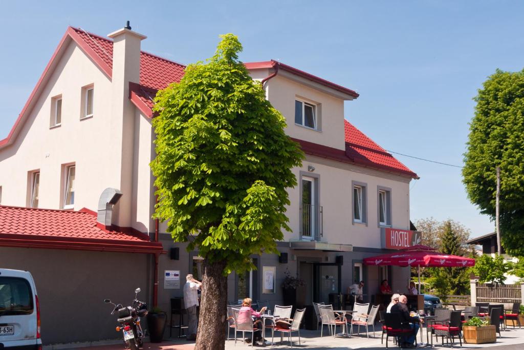 un árbol frente a un edificio con gente sentada en las mesas en Hostel Plus Caffe en Petrovče