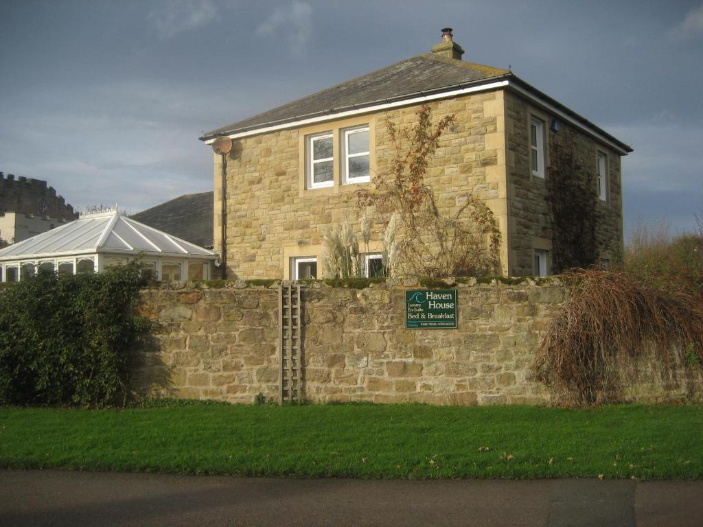 a house behind a brick wall with a sign on it at Haven House B&B in Beadnell