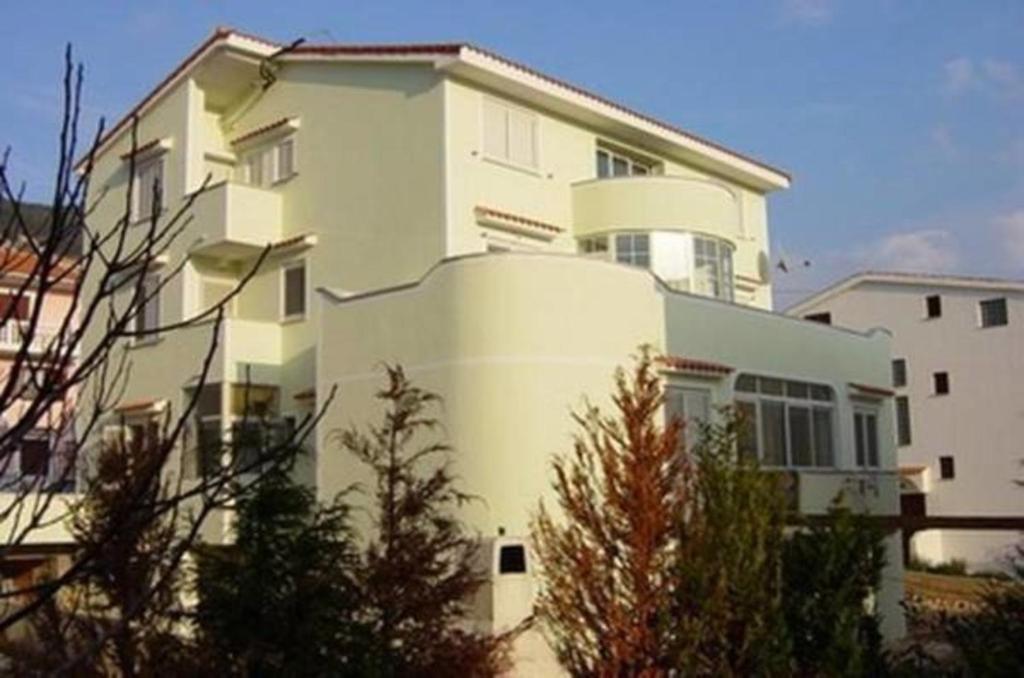 een groot wit gebouw met bomen ervoor bij Apartments Luka 2 in Baška