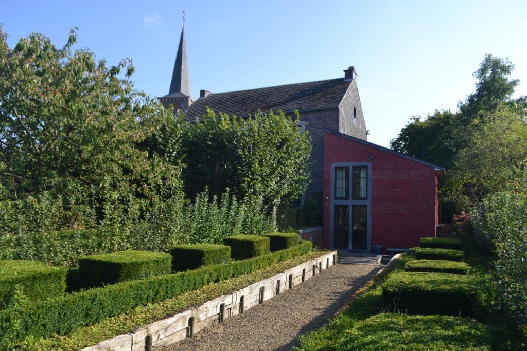 a red building with a garden with trimmed bushes at Le Presbytere in Tourinne