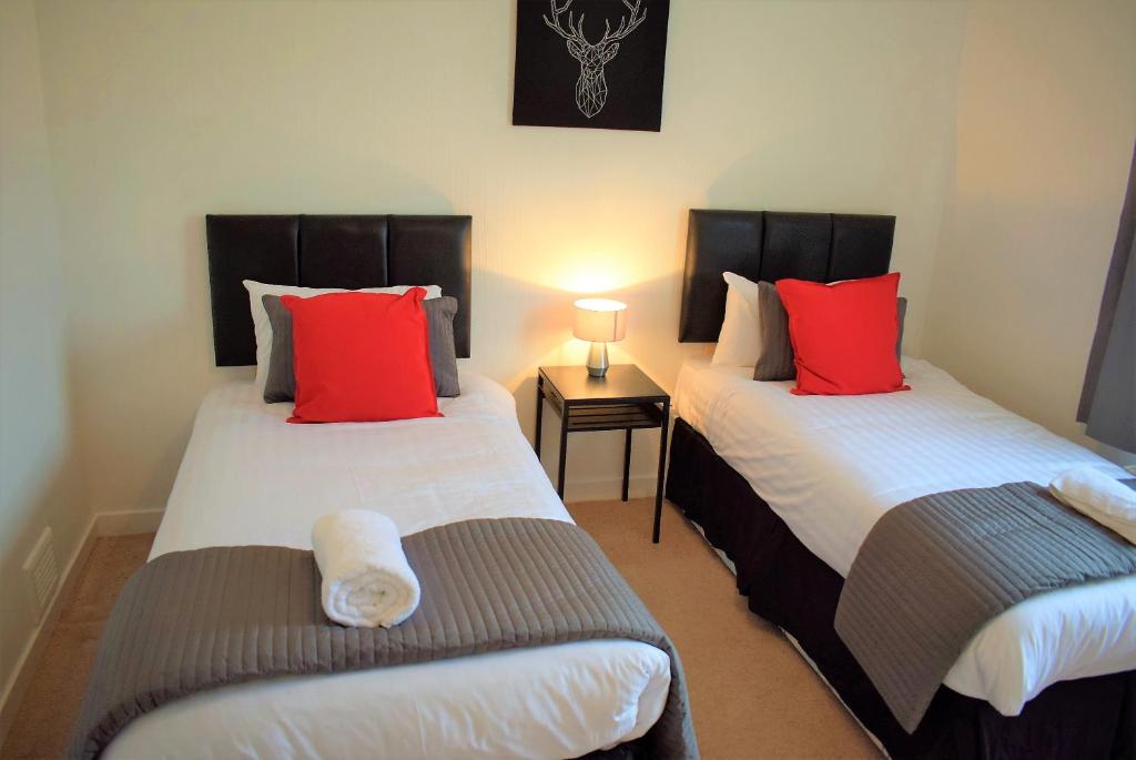 2 bedden met rode kussens in een kamer bij Kelpies Serviced Apartments MacGregor- 2 Bedrooms in Grangemouth