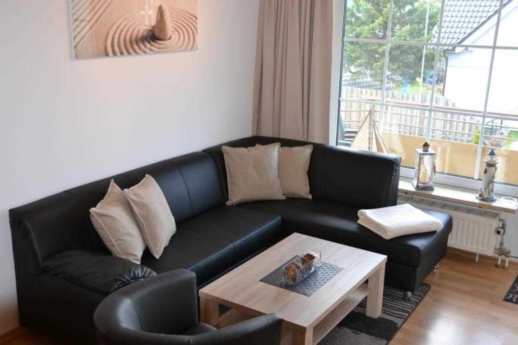 ein Wohnzimmer mit einem schwarzen Ledersofa und einem Couchtisch in der Unterkunft (DKK11) Ferienwohnung Strandburg in Niendorf