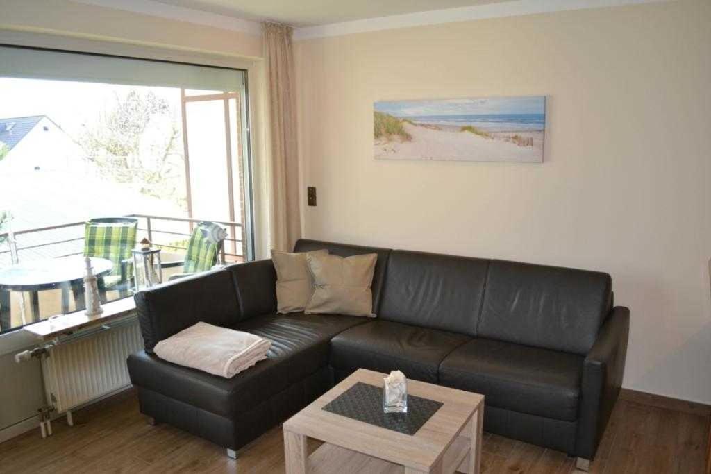 ein Wohnzimmer mit einem schwarzen Ledersofa und einem Tisch in der Unterkunft (DKK1d) Ferienwohnung Seemöwe in Niendorf