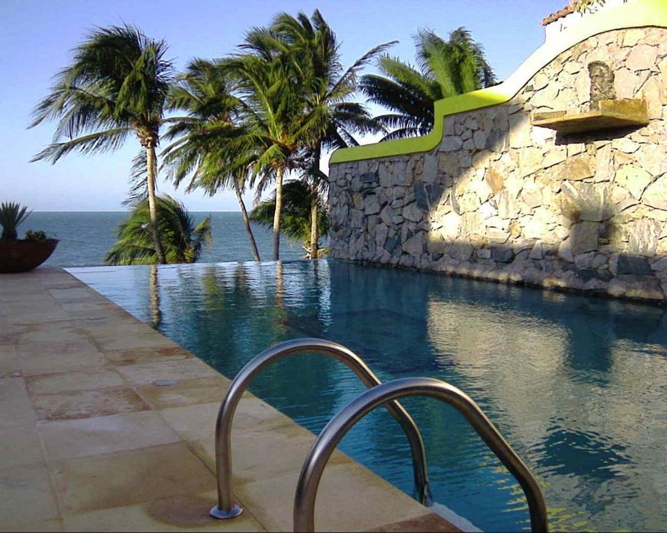 a swimming pool with palm trees and a stone wall at Barbanera Club & Hotel de Charme in Caucaia