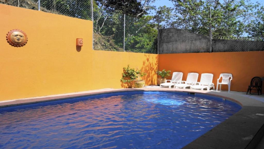 a swimming pool with white chairs and a yellow wall at La Vivienda Villa in Santa Cruz Huatulco
