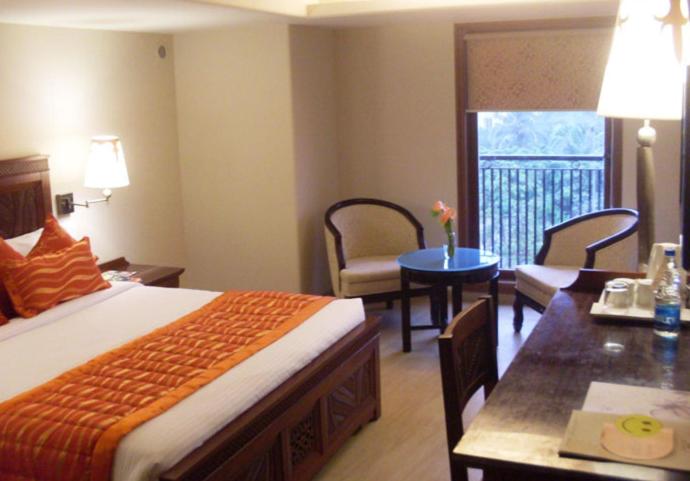 ムンバイにあるHotel Sai Innのベッド、テーブル、椅子が備わるホテルルームです。