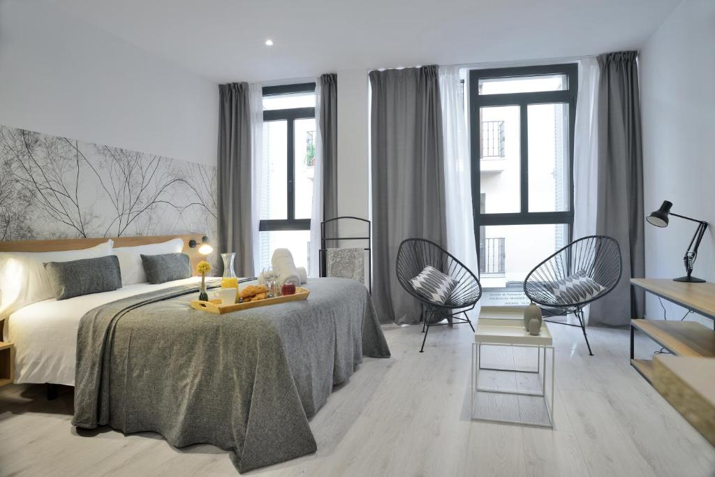 um quarto com uma cama, 2 cadeiras e janelas em Aspasios Atocha Apartments em Madrid