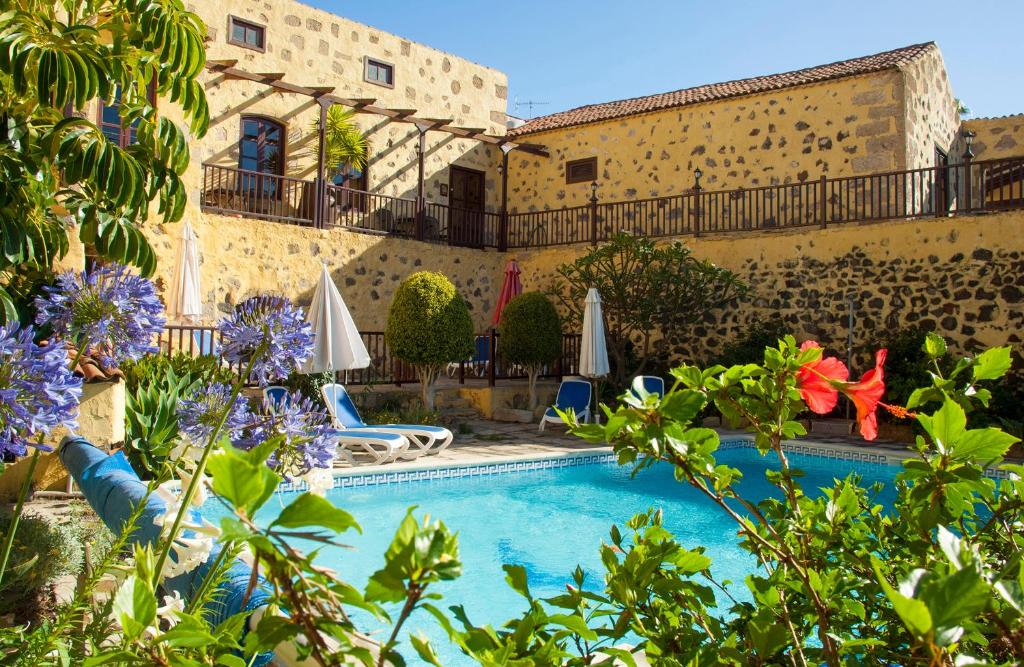 a pool in front of a building with umbrellas and flowers at La Bodega Casa Rural, Tenerife. in San Miguel de Abona