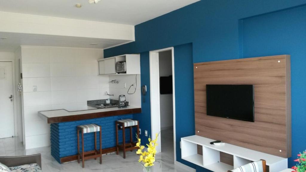 a living room with a blue wall and a kitchen at Farol Barra Flat completo e bem localizado in Salvador