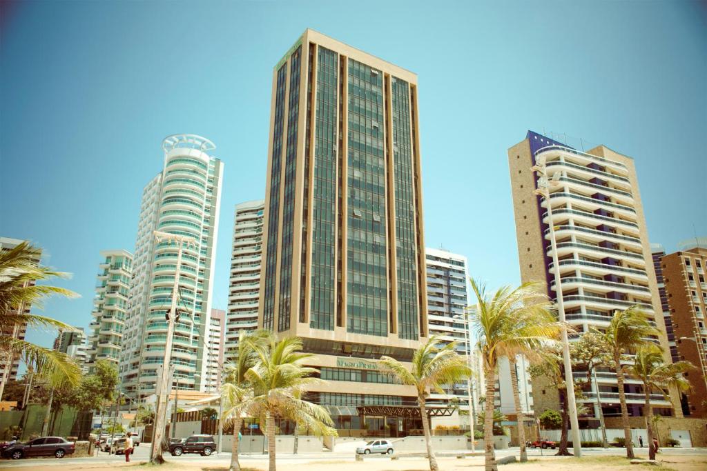 a group of tall buildings in a city with palm trees at Magna Praia Hotel in Fortaleza