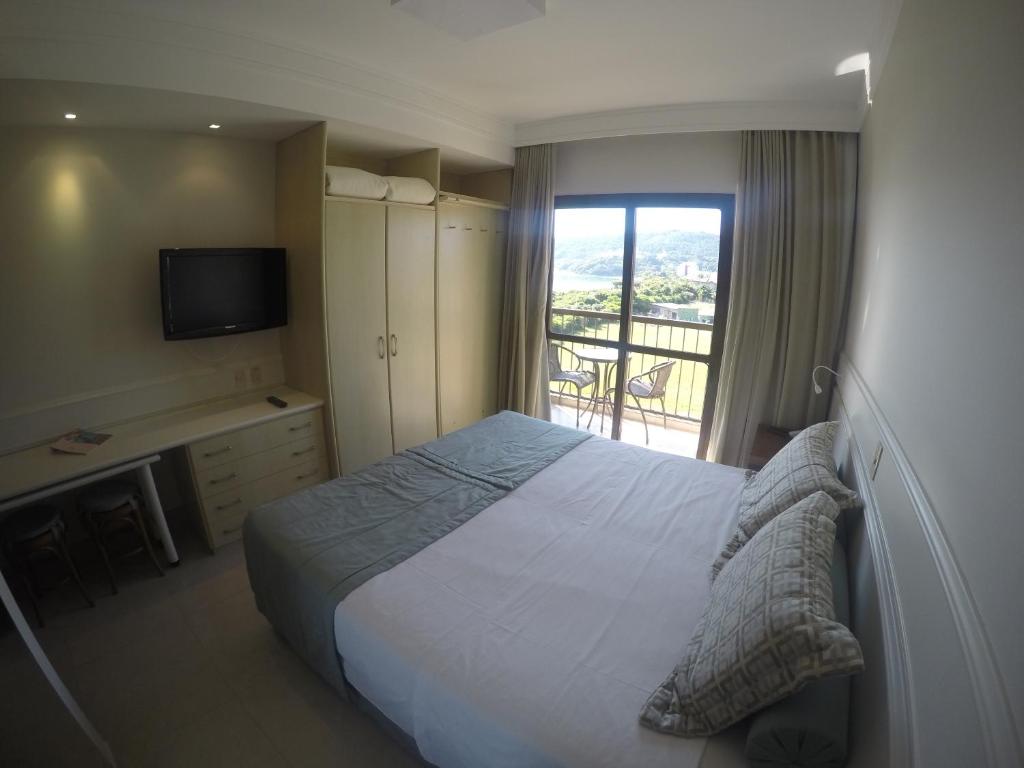 een slaapkamer met een bed, een televisie en een balkon bij Studio em Jurerê - Pé na Areia in Florianópolis