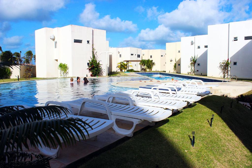 a swimming pool with white lounge chairs in front of a building at Paraiso de Maracajau 4 in Maracajaú
