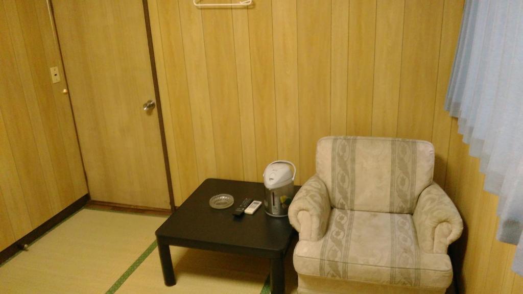 a room with a chair and a table with a lamp at Minshuku Takahashi Kashibuneten in Maisaka