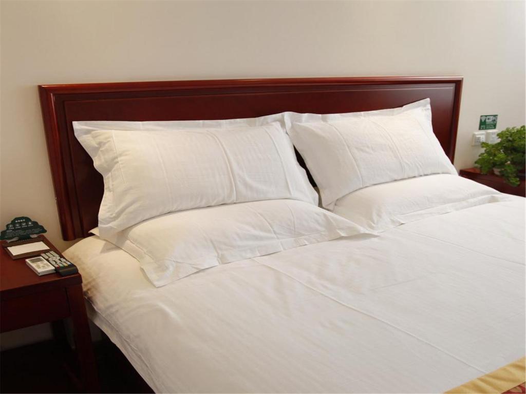 a white bed with white pillows and a wooden headboard at Greentree Inn Shanghai Zhongshan Hutai Business Hotel in Shanghai