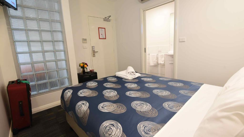 a bedroom with a bed with a blue comforter and a window at Hostel 109 Flashpackers in Adelaide