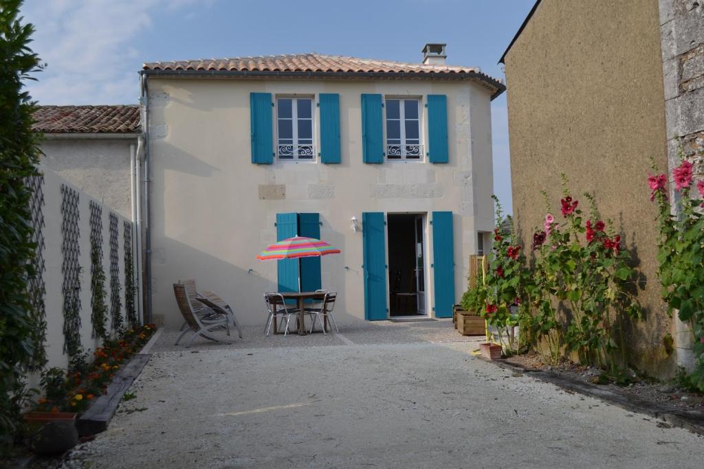 une maison blanche avec des volets bleus et une table avec un parasol dans l'établissement Gite Du Chai, à Chenac Saint Seurin D'uzet