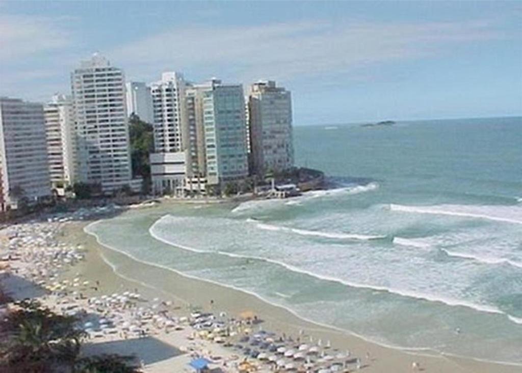 einen Strand mit Sonnenschirmen, Meer und Gebäuden in der Unterkunft Flat em Pitangueiras - Guarujá in Guarujá