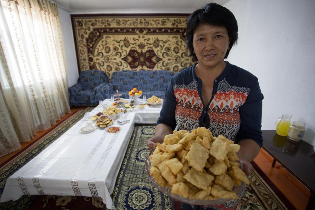 a woman holding a bowl of potato chips in front of a table at Nurgul in Bokonbayevo