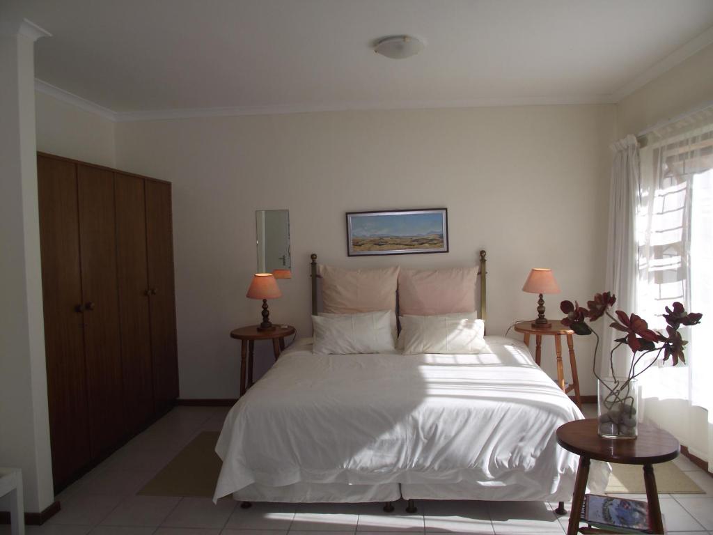 a bedroom with a white bed with two tables and two lamps at Hermanus At Rikis Self Catering in Hermanus