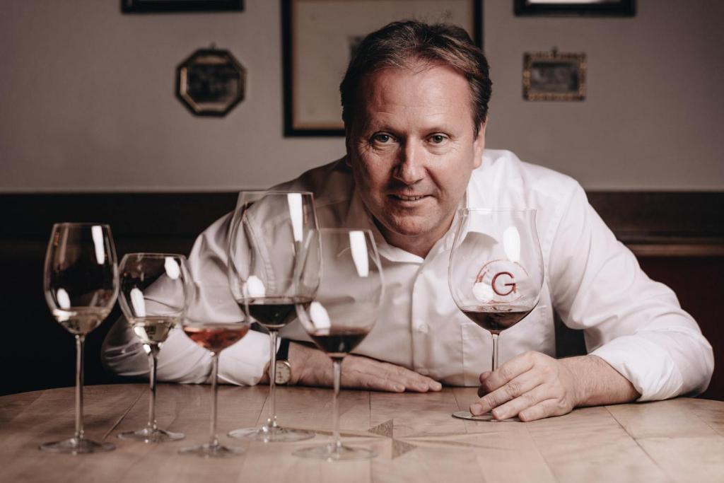 a man sitting at a table with four wine glasses at DER GREIL - Wein & Gourmethotel in Söll