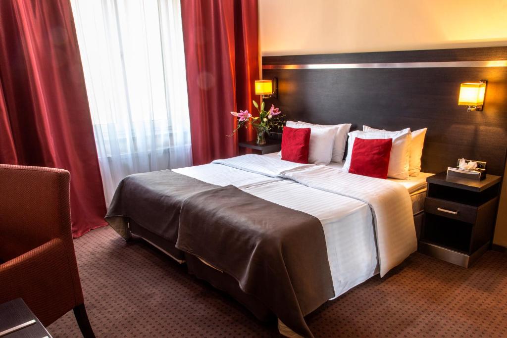 una habitación de hotel con una cama grande con cortinas rojas en Delta In, en Dzierżoniów