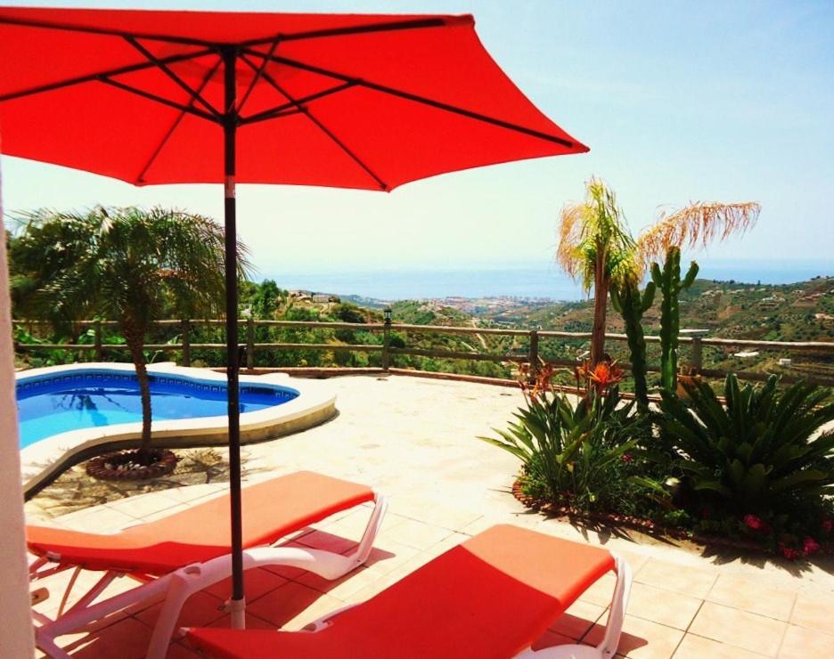 een patio met een rode parasol en stoelen en een zwembad bij Peperent Villa Buenavista in Torrox